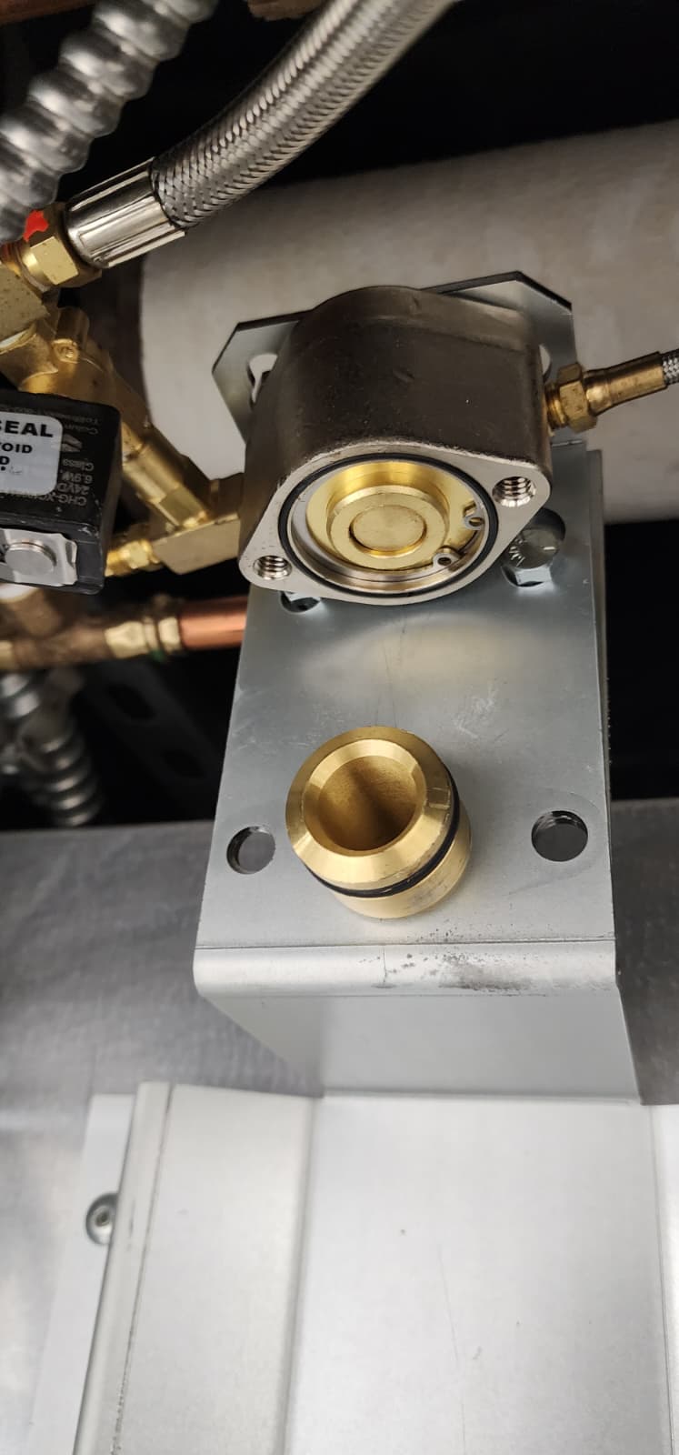 Close-up of the wiring connector and pneumatic fitting on a CaptiveAire cylinder release actuator showing labeled terminals, a sealed strain relief, and the SS hose coupling that runs back to the control panel