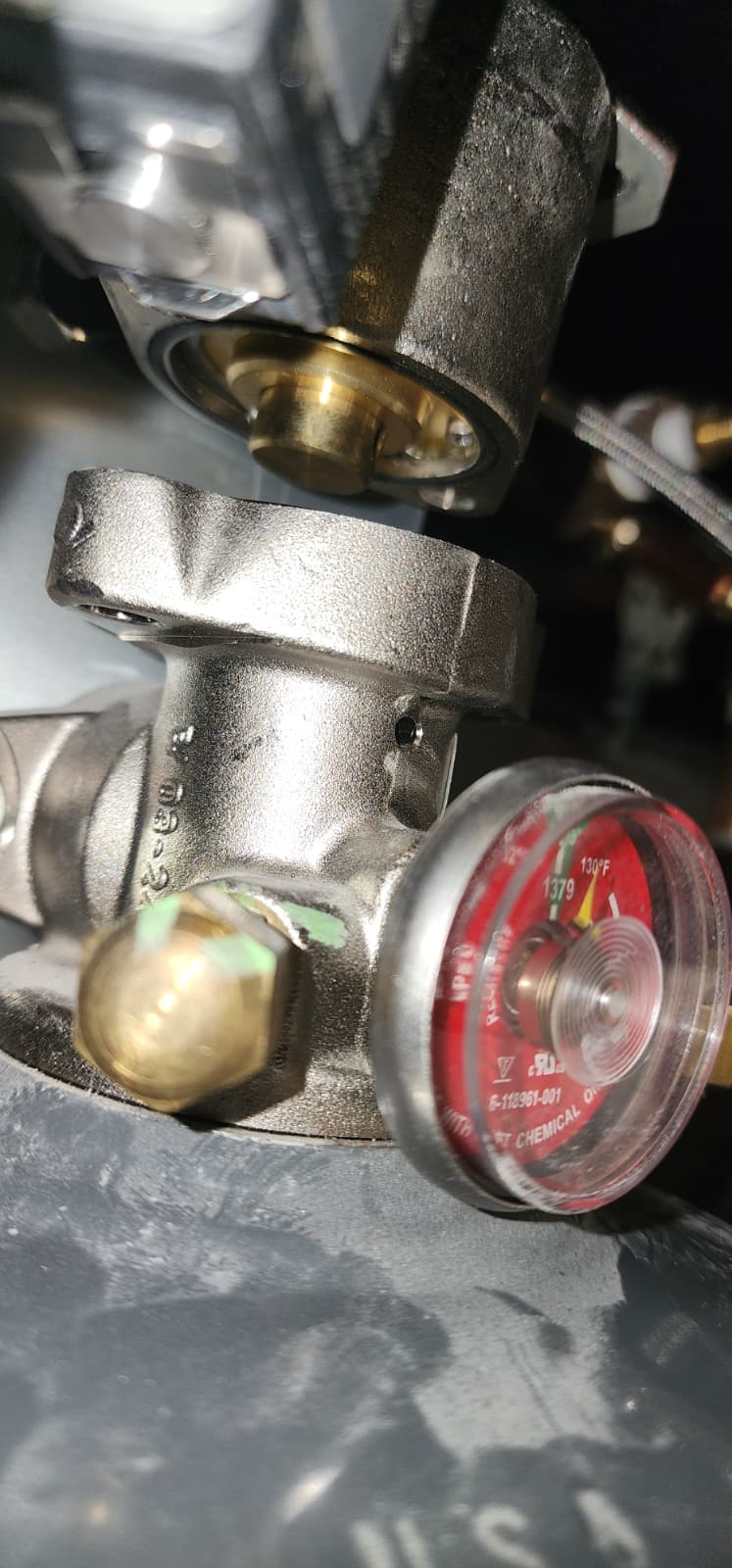 A CaptiveAire cylinder release actuator with the pneumatic hose detached from the cylinder valve and the safety pin visible through the actuator body — the cylinder is fully isolated from the actuation circuit prior to a discharge-output test