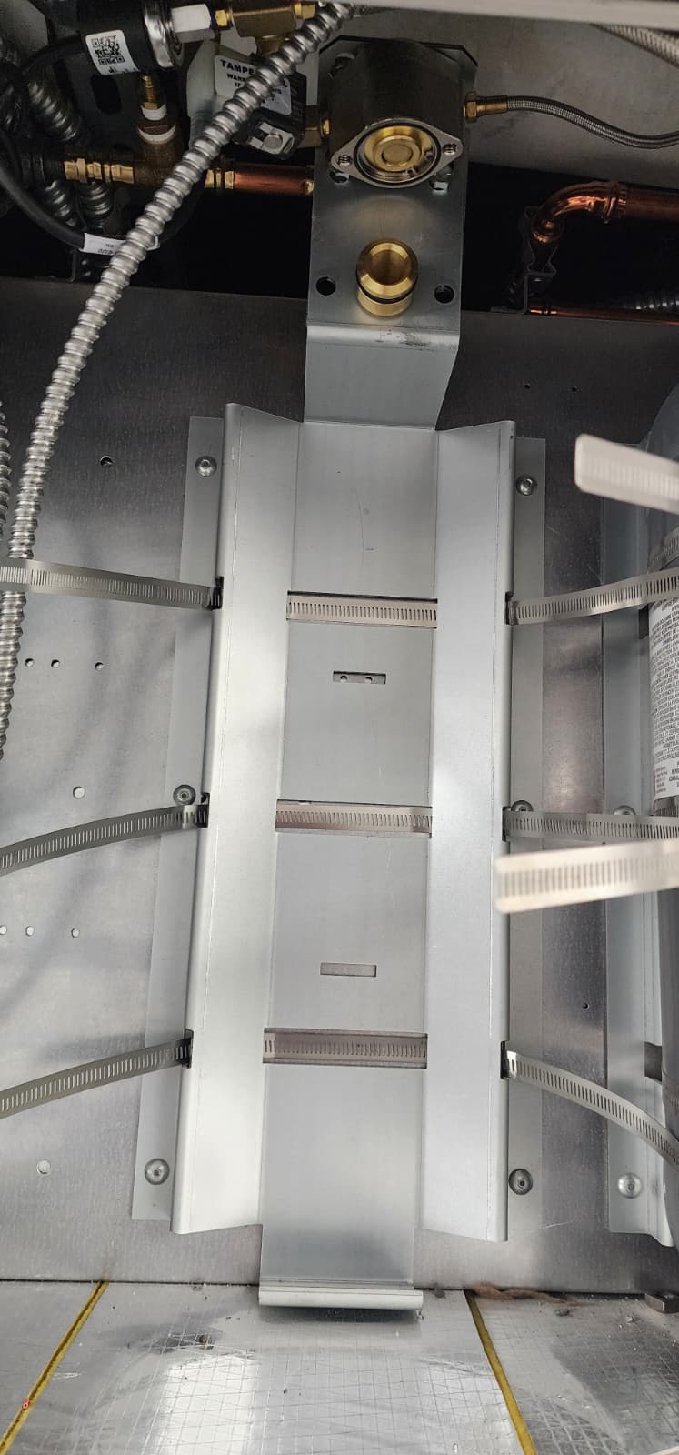 Empty CaptiveAire cylinder bay inside a stainless cabinet showing the integrated mounting saddle and bracket, agent piping connection point, and signal wiring stub at the back wall — the cylinder has been removed for service
