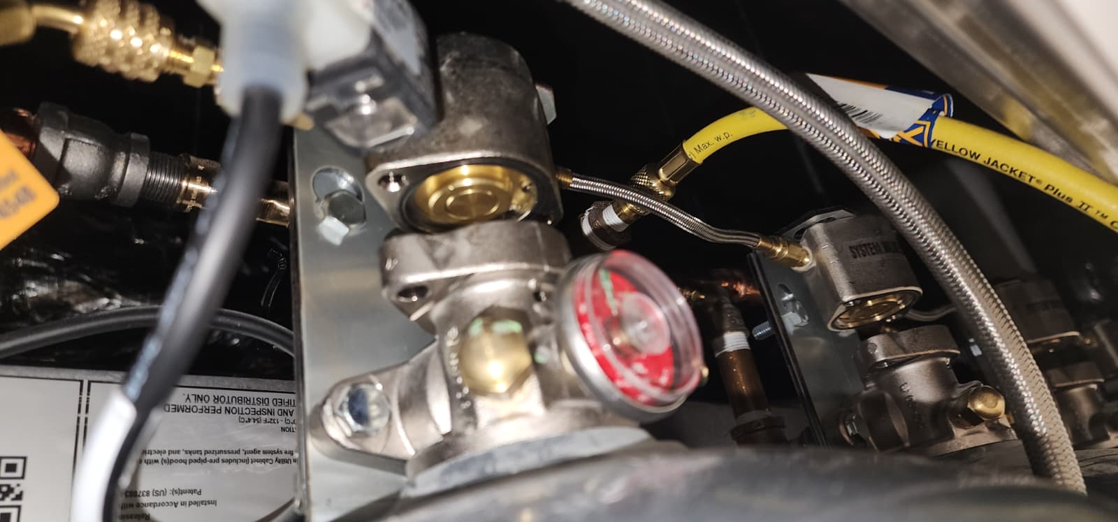 Yellow regulated nitrogen test hoses tee'd into the cylinder actuation circuit through a brass manifold, with a pressure gauge mid-line showing applied test pressure during the discharge-output verification