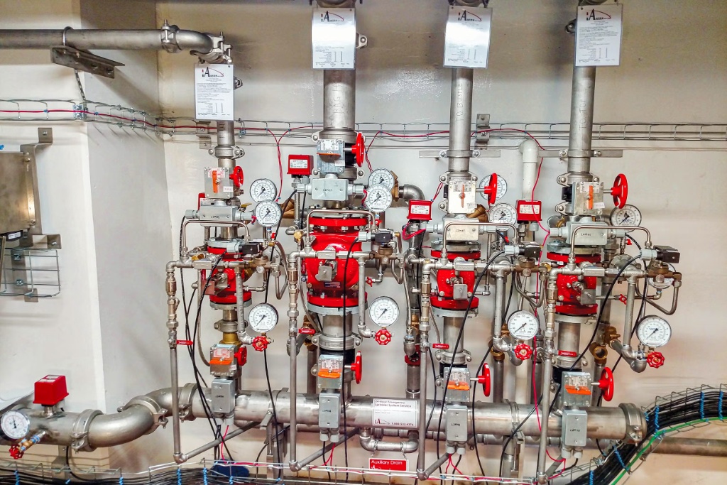 Bank of four deluge valves in a pump-room manifold with individual control wheels, pressure gauges, electric release trims, and supervised wiring to each valve