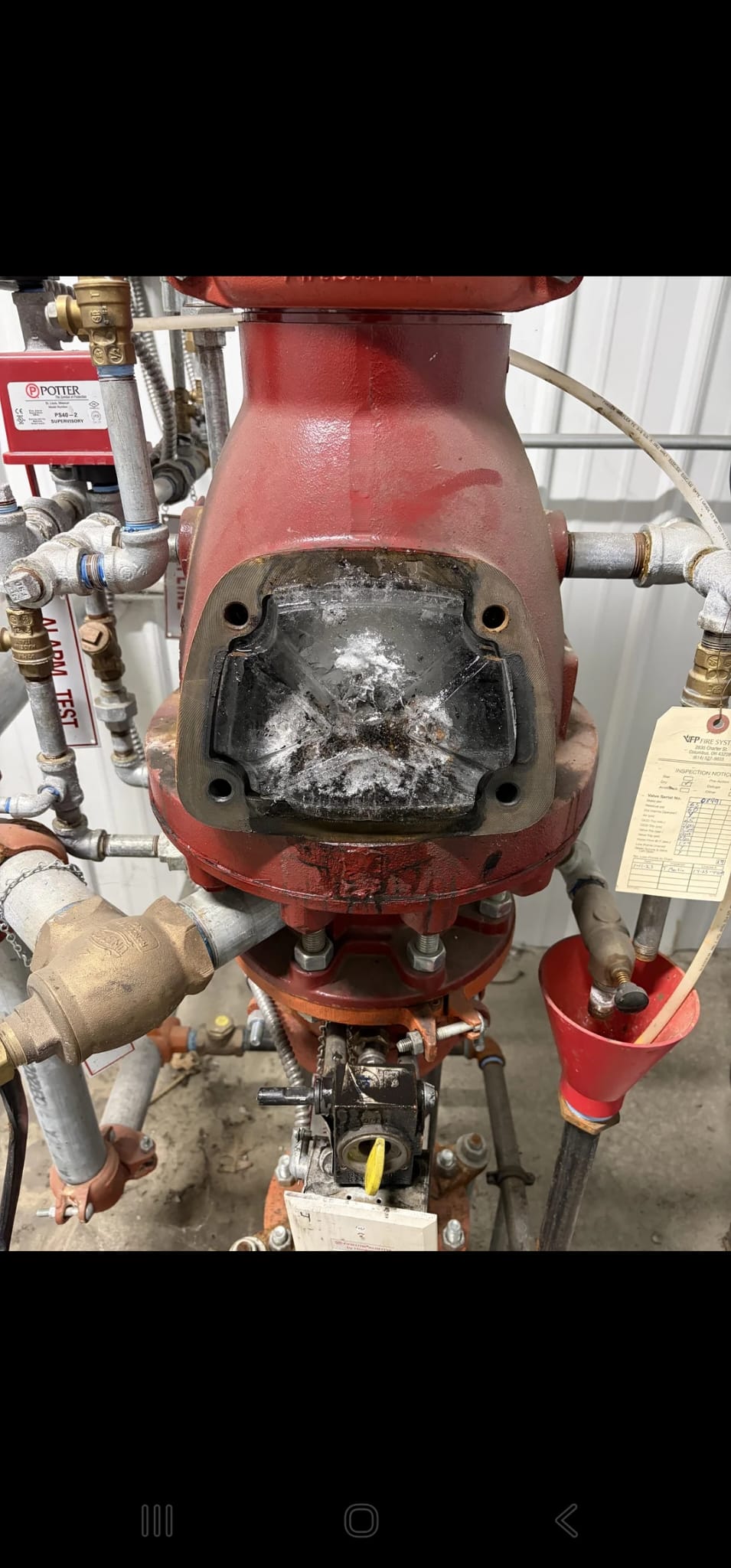 Interior photograph of a dry pipe valve with the cover plate removed during internal inspection, showing extensive internal build-up of ice and frost on the clapper seat and valve body — white frosted surfaces and frozen condensate coating the sealing face