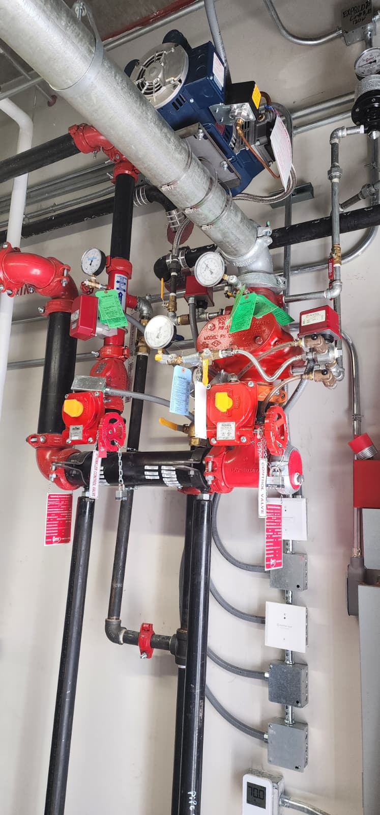 Dry pipe valve assembly with wall-mounted air compressor, galvanized system piping, supervisory pressure gauges, control valves with tamper switches, pressure switch enclosures, and drum drip drain