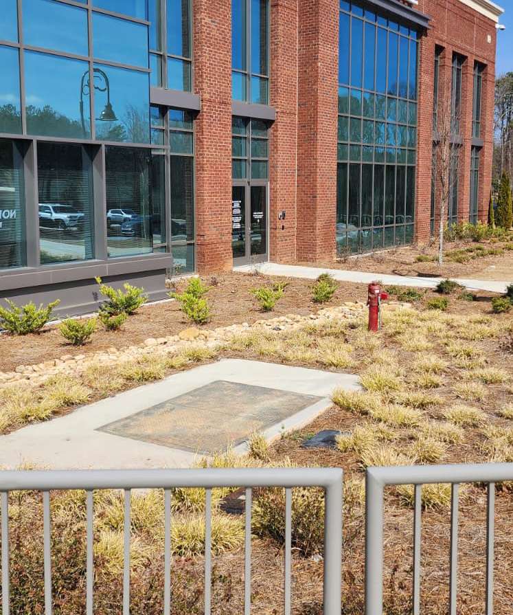 A red post indicator valve (PIV) installed in the landscaped front yard of a commercial building in Snellville, Georgia — above-ground steel post with the OPEN/SHUT indicator window and a padlocked handwheel, adjacent to a concrete underground vault access pad