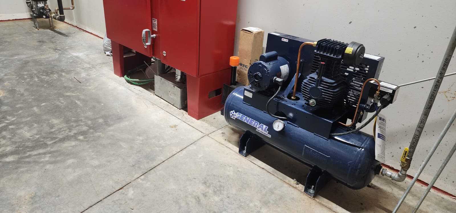 General Air Products oil-less tank-mounted air compressor installed next to a red Viking dry pipe valve riser — typical dry system configuration in a commercial facility