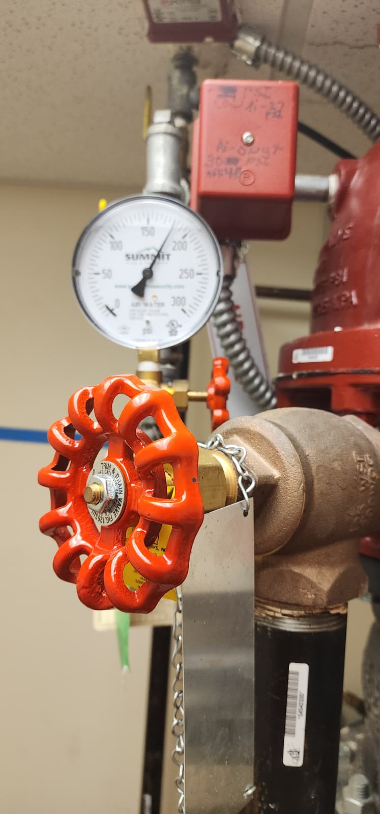 Dry pipe valve trim close-up showing Summit air/water pressure gauge 0-300 psi, red drain handwheel trim valve, Potter pressure switch mounted above, and electrical conduit running to the FACP