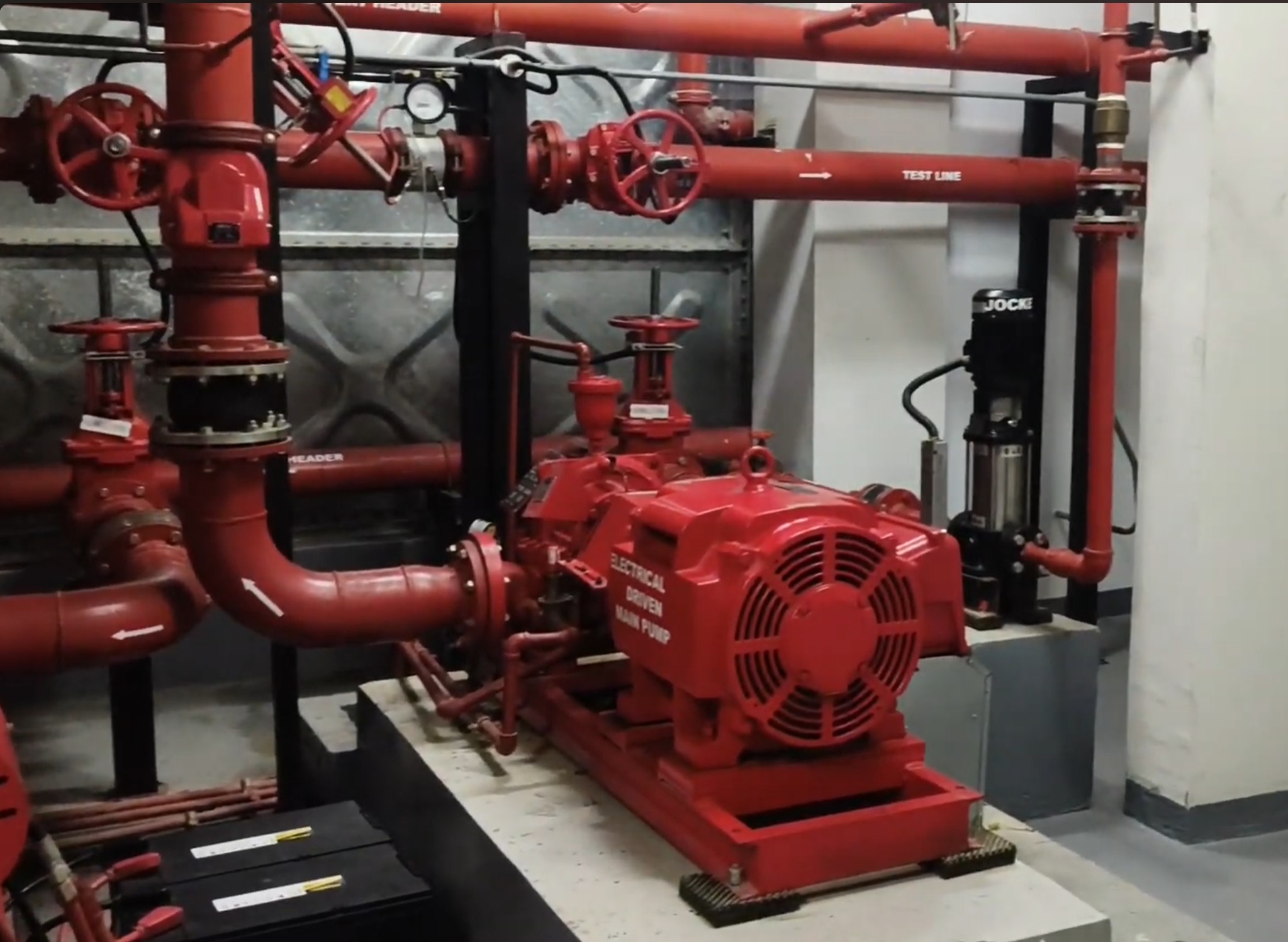 Fire pump room — electric driven main pump labeled 'ELECTRICAL DRIVEN MAIN PUMP' with test header, test line, OS&Y valves, jockey pump (black, right), and suction/discharge piping