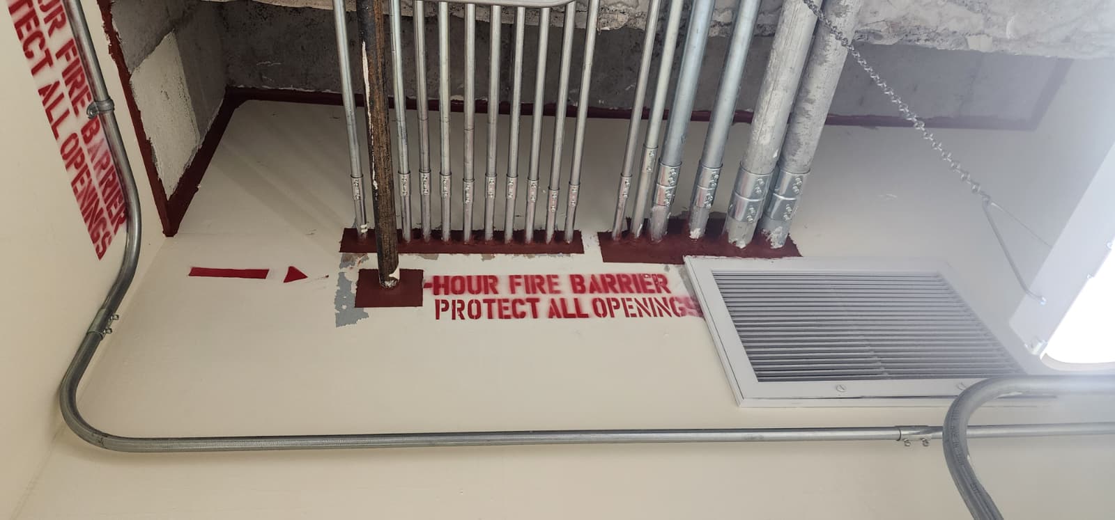 Fire barrier rated wall with conduit penetrations sealed with red firestop and 'HOUR FIRE BARRIER - PROTECT ALL OPENINGS' stencil
