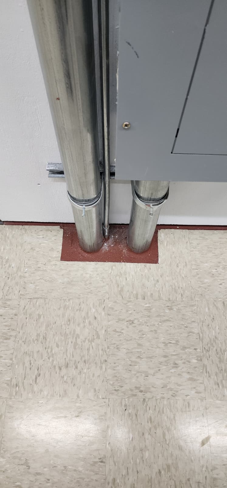 Floor penetration with conduit sealed by red intumescent firestop around the base