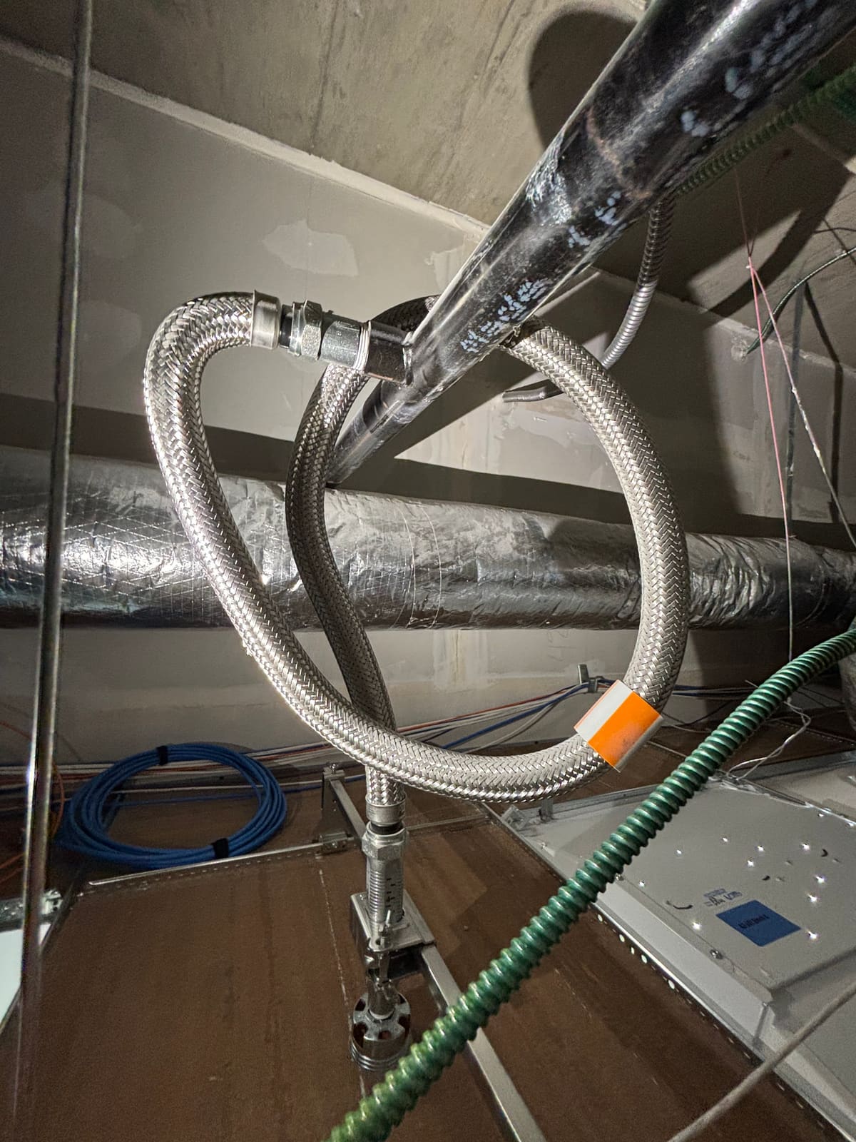 Braided flexible sprinkler hose coiled into a complete 360-degree loop above a suspended ceiling