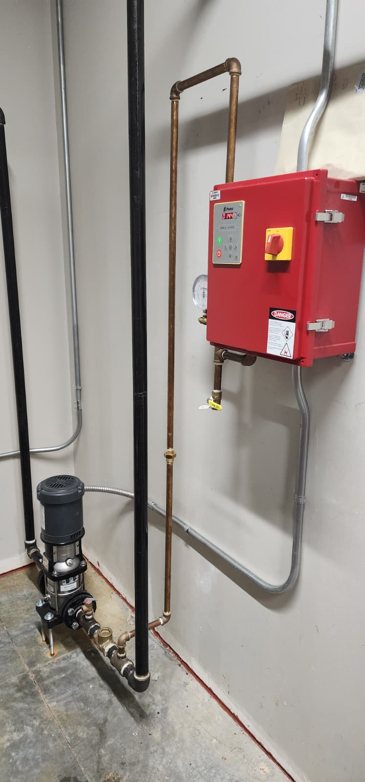 Wall-mounted Firetrol jockey pump controller with LED pressure display, red-e enclosure, digital setpoints, and emergency stop switch, next to the small vertical multi-stage jockey pump below and copper sensing line above