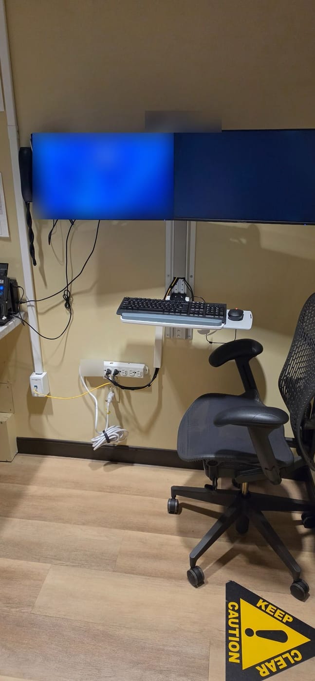 A power strip fastened to the wall beneath a wall-mounted computer workstation
