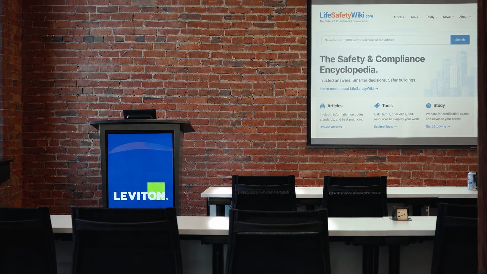 Visual concept: LifeSafetyWiki.com displayed on a presentation screen beside Leviton branding in a brick conference room