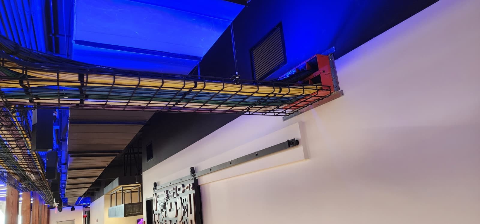 Overhead structured network cabling tray running through Leviton's experience center under blue accent lighting