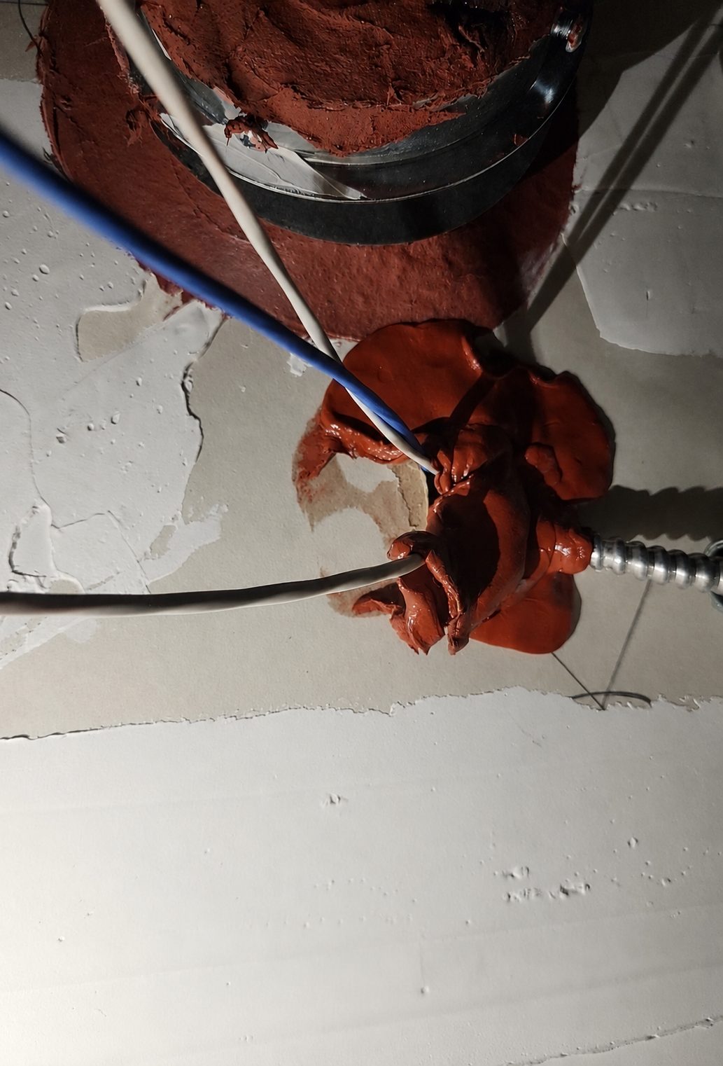 Above the ceiling: putty pad blobbed around cables and MC cable at a fire-rated wall penetration, drywall peeling around edges