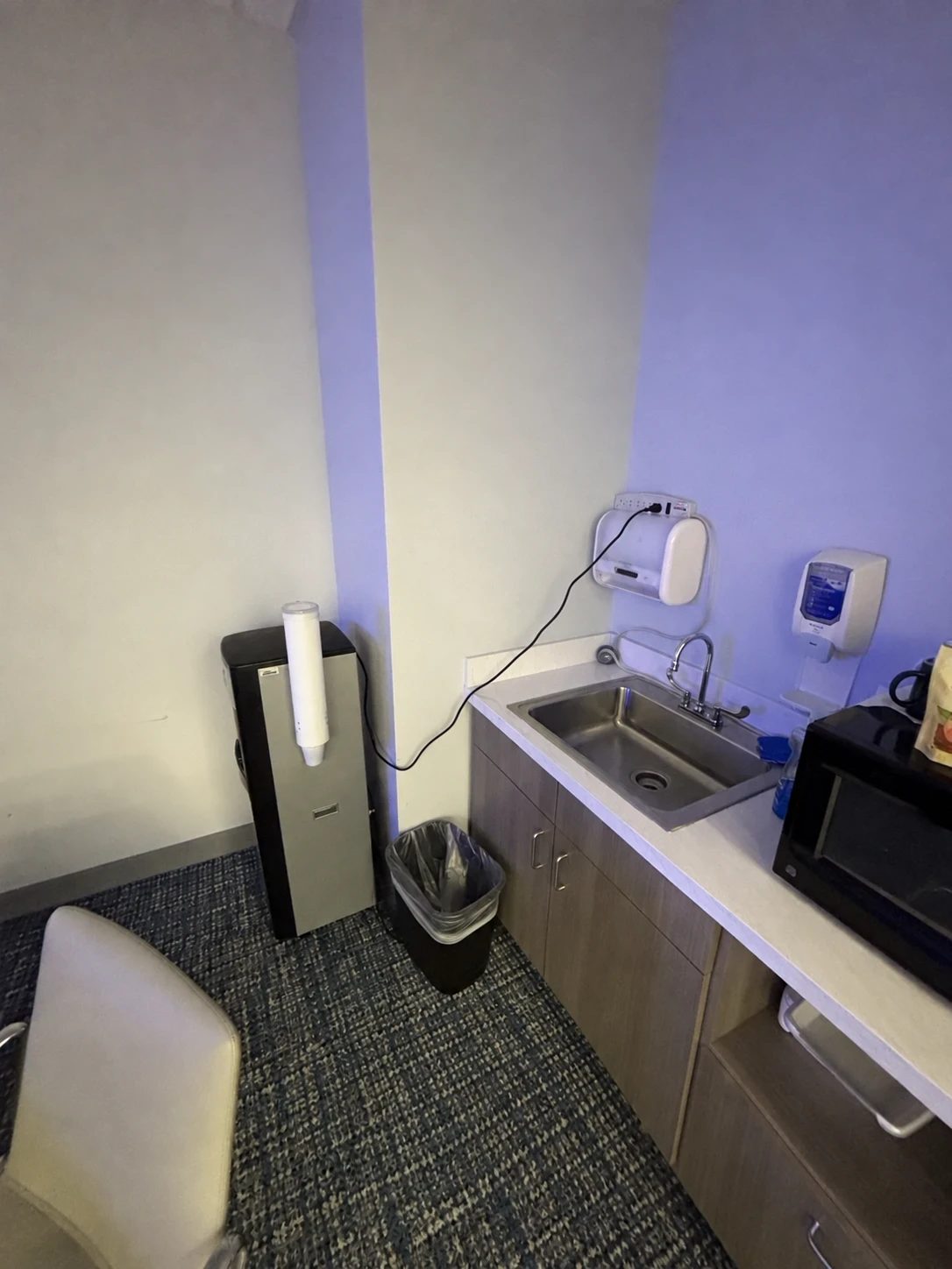 A wall-mounted electrical device with a cord running down to just above a break-room sink and faucet