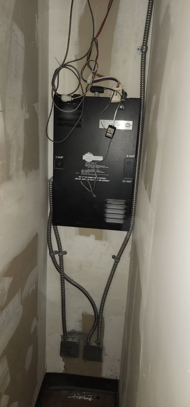 Black fire door operator controller box with labeled circuit provisions and flexible metallic conduit connections entering the enclosure
