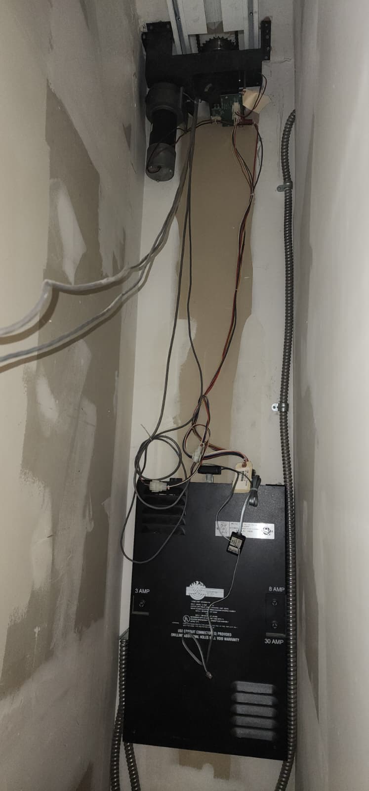 Motor drive gear assembly at the top of a fire door housing and the operator controller below it, connected by flexible metallic conduit