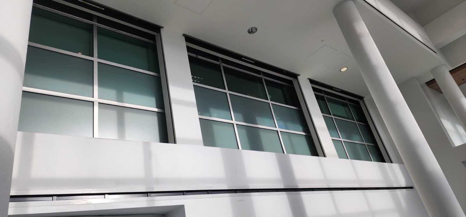 Three large vertical sliding fire doors with rated glazing panels in a hospital atrium, shown partially in the raised open position with the overhead track housing above