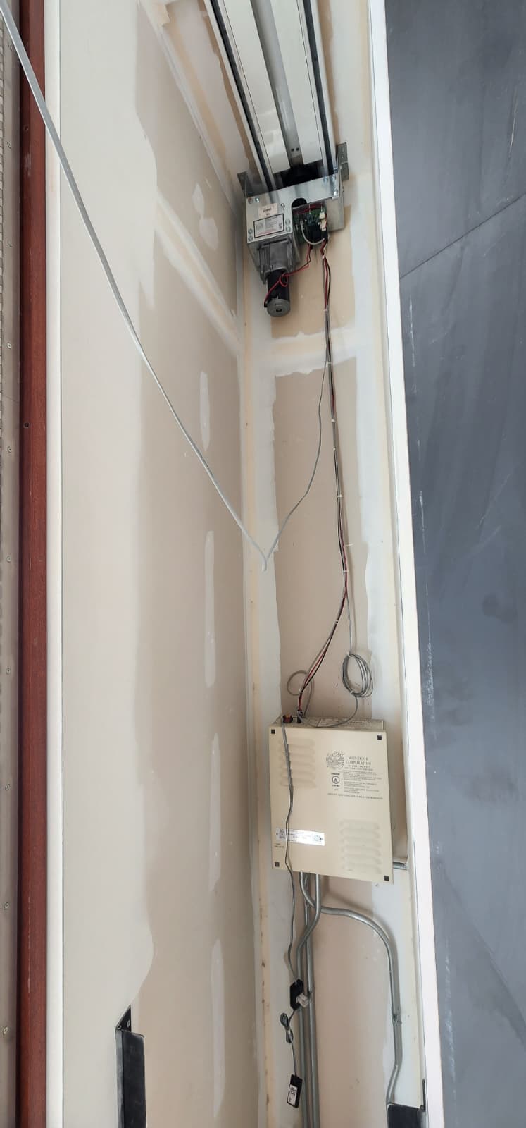 WON-Door fire door motor operator head mounted at the top of the track housing, with the WON-Door Corporation controller box mounted below it and wiring connecting the two components