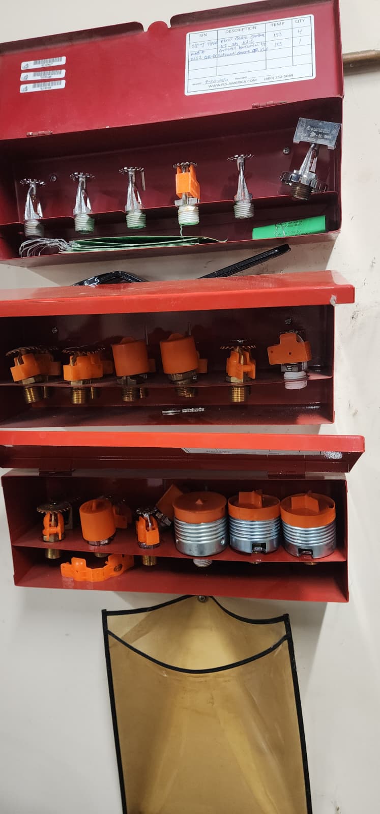 Three stacked spare sprinkler cabinets showing variety of head types — pendants, uprights, sidewalls, concealed, recessed, ESFR, and quick-response — of different temperature ratings and finishes