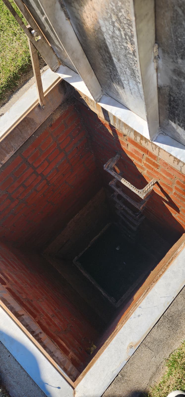 Open brick-lined valve vault below grade with an iron ladder descending to the valve chamber — typical for an underground gate valve or FDC check-valve pit
