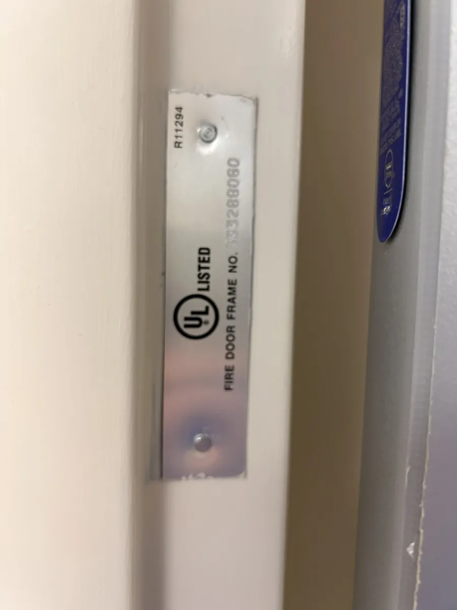 A UL Listed Fire Door Frame label riveted to a painted steel frame, with no hourly rating