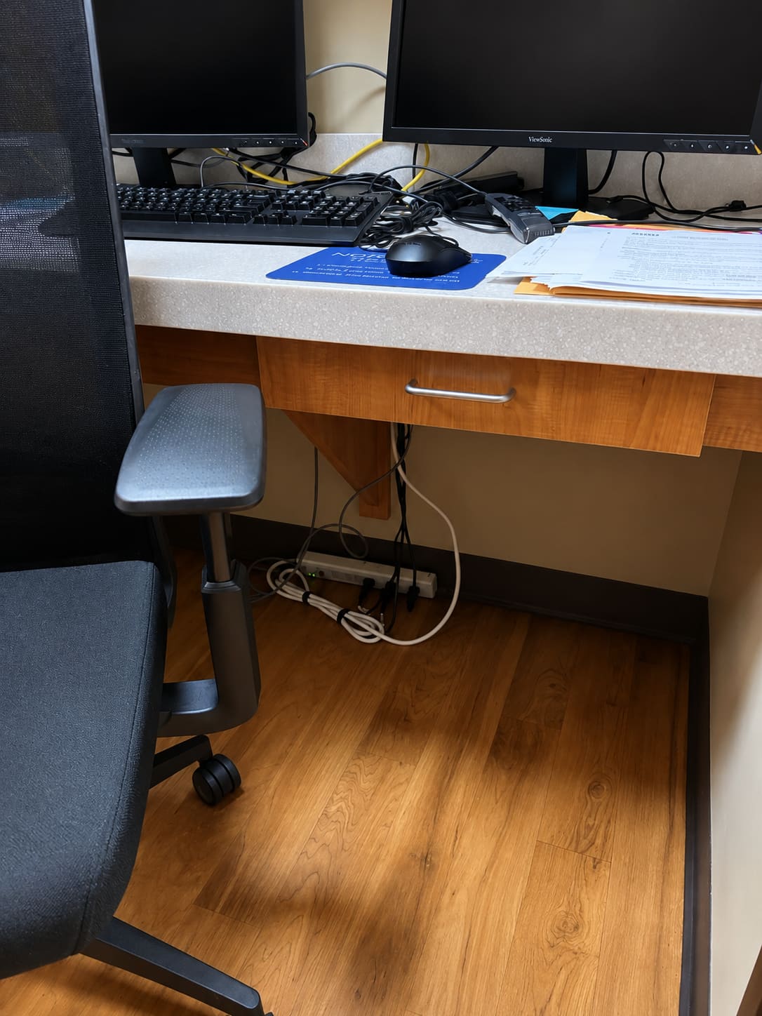 A workstation with a power strip lying loose on the floor beneath the desk, cords bundled around it